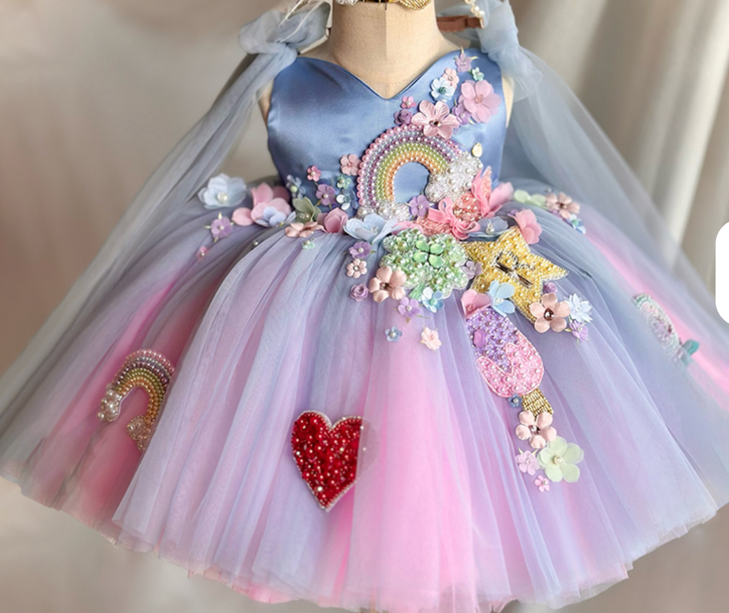 Colorful children's dress with floral decorations and a rainbow design on a mannequin.