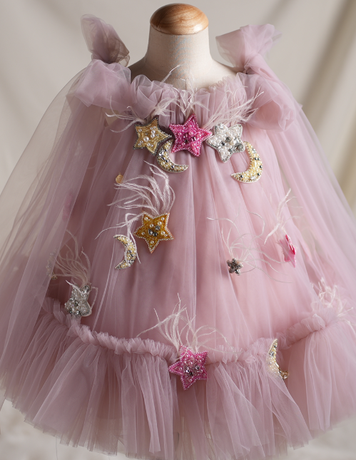 Pink tulle dress with star and moon embellishments on a mannequin against a neutral background