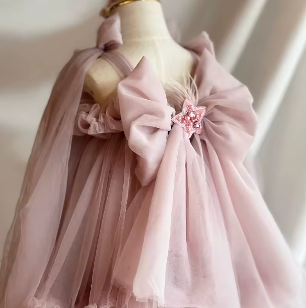 Pink dress with a large bow and decorative element on a mannequin against a neutral background
