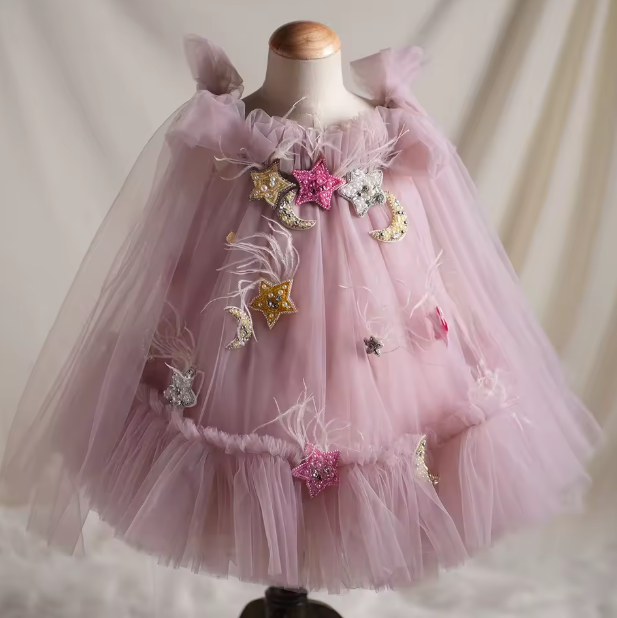 Pink tulle dress with star and moon embellishments on a mannequin against a neutral background