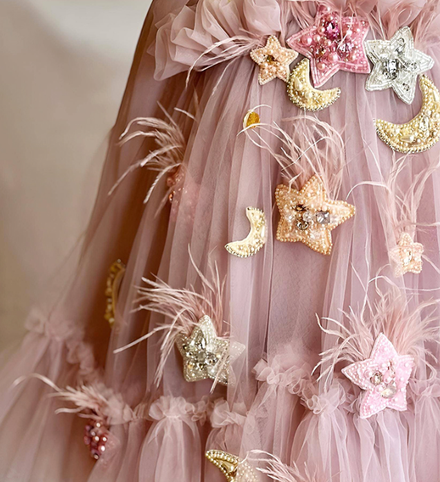 Pink tulle dress with decorative stars and moons on a plain background