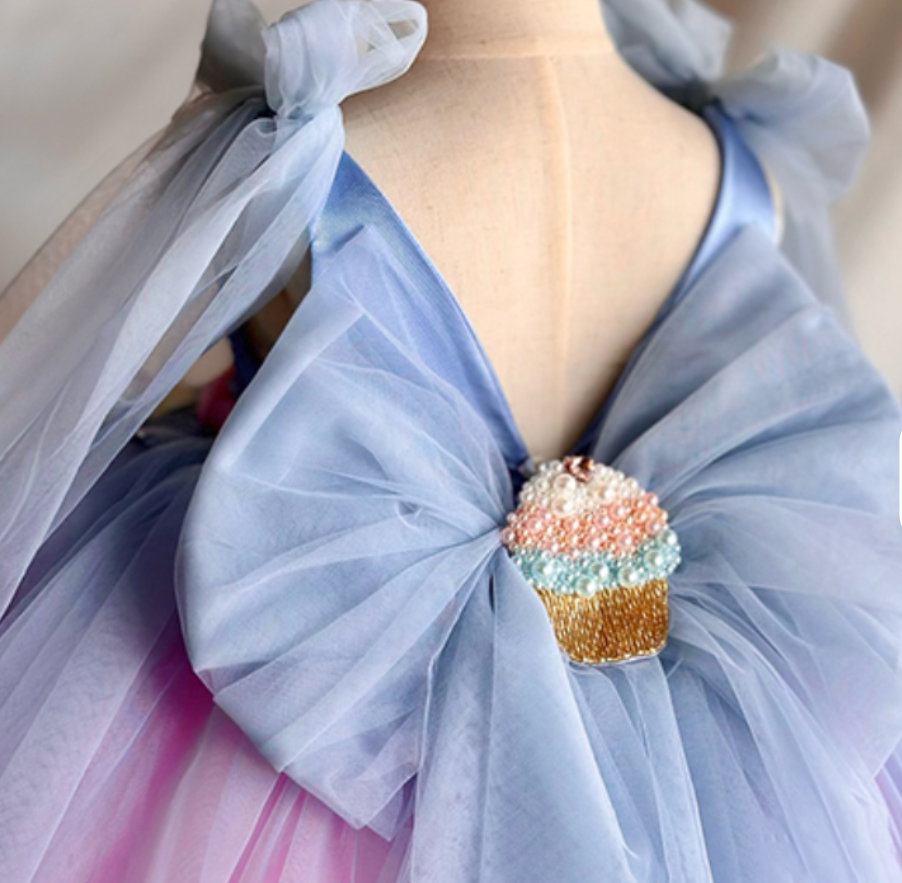 Mannequin wearing a light blue dress with a large bow and a colorful cupcake brooch.