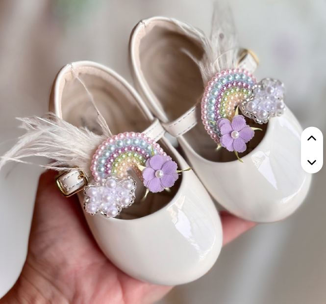 White baby shoes with decorative elements held by a hand against a neutral background