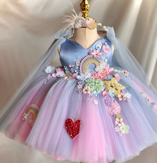 Colorful children's dress with floral and rainbow decorations on a mannequin against a neutral background.