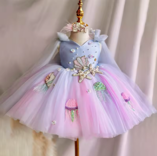 Colorful children's dress with floral and candy designs on a mannequin against a neutral background.